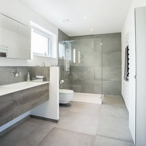 Ein modernes Badezimmer mit grauen Fliesen, einer großen Dusche und einem eleganten Waschbecken aus Holz.