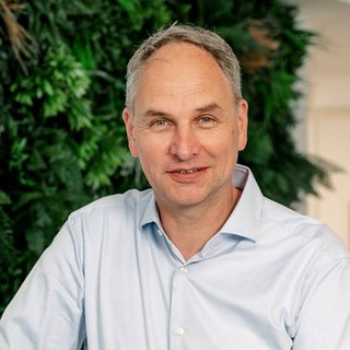 Portrait eines freundlichen Mannes in einem modernen Büro Vor einer lebendigen Pflanzenkulisse sitzt ein Mann, der mit einem offenen Lächeln in die Kamera schaut.