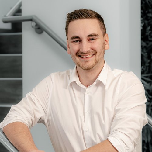 Der Mann trägt ein weißes Hemd und strahlt Selbstbewusstsein aus, während er an einer Treppe steht.