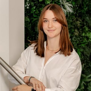 Elegante Porträtaufnahme einer Frau in heller Bluse In einem modernen Raum posiert eine Frau in einem weißen Hemd, ihre entspannte Haltung strahlt Selbstbewusstsein und Freundlichkeit aus.