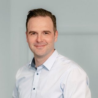 Professionelles Porträt eines lächelnden Mannes in Hemd Der Mann hat kurzes, dunkles Haar und strahlt Selbstbewusstsein aus, während er in die Kamera schaut.